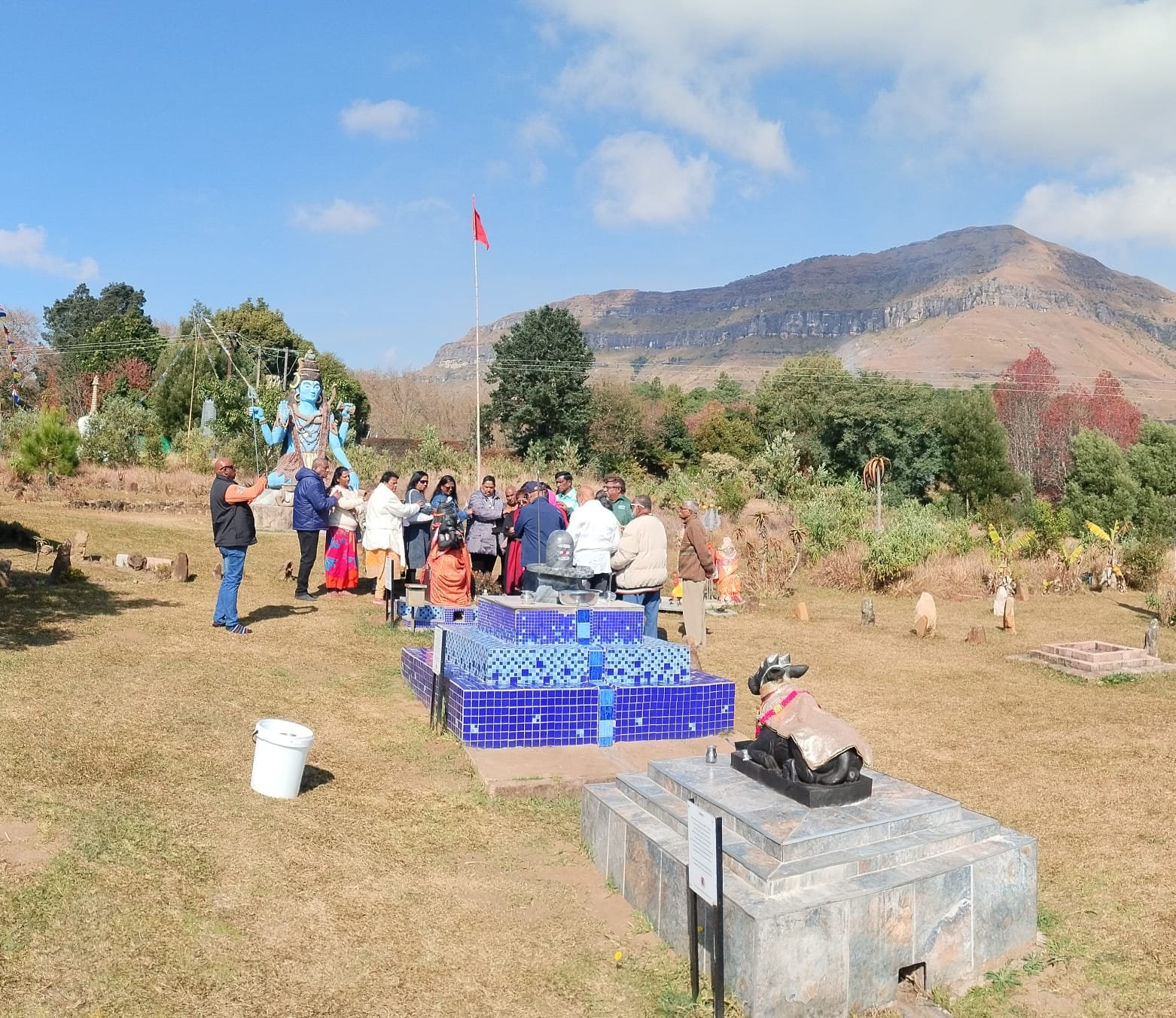 Devotees gathered near the lingam and Nandi statue with mountains behind