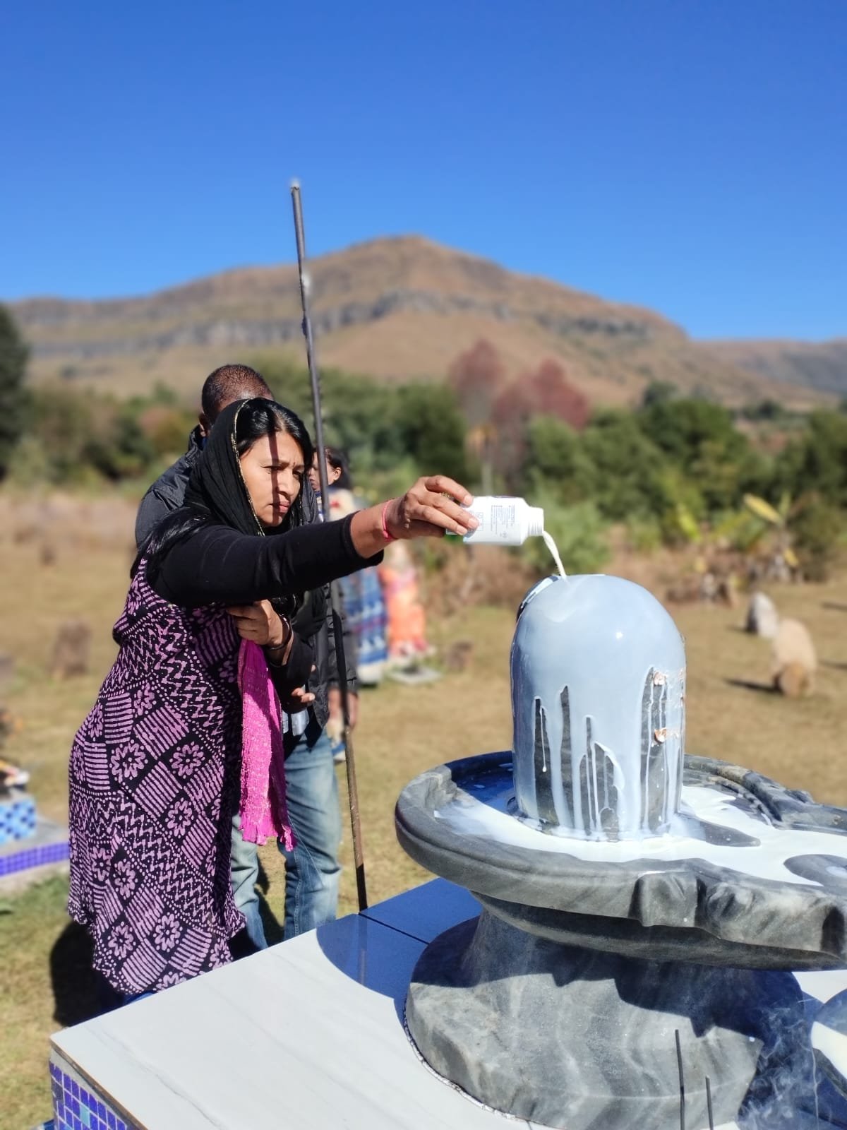 Devotee performing abhishekam, pouring milk over the Shiva lingam, with mountains behind